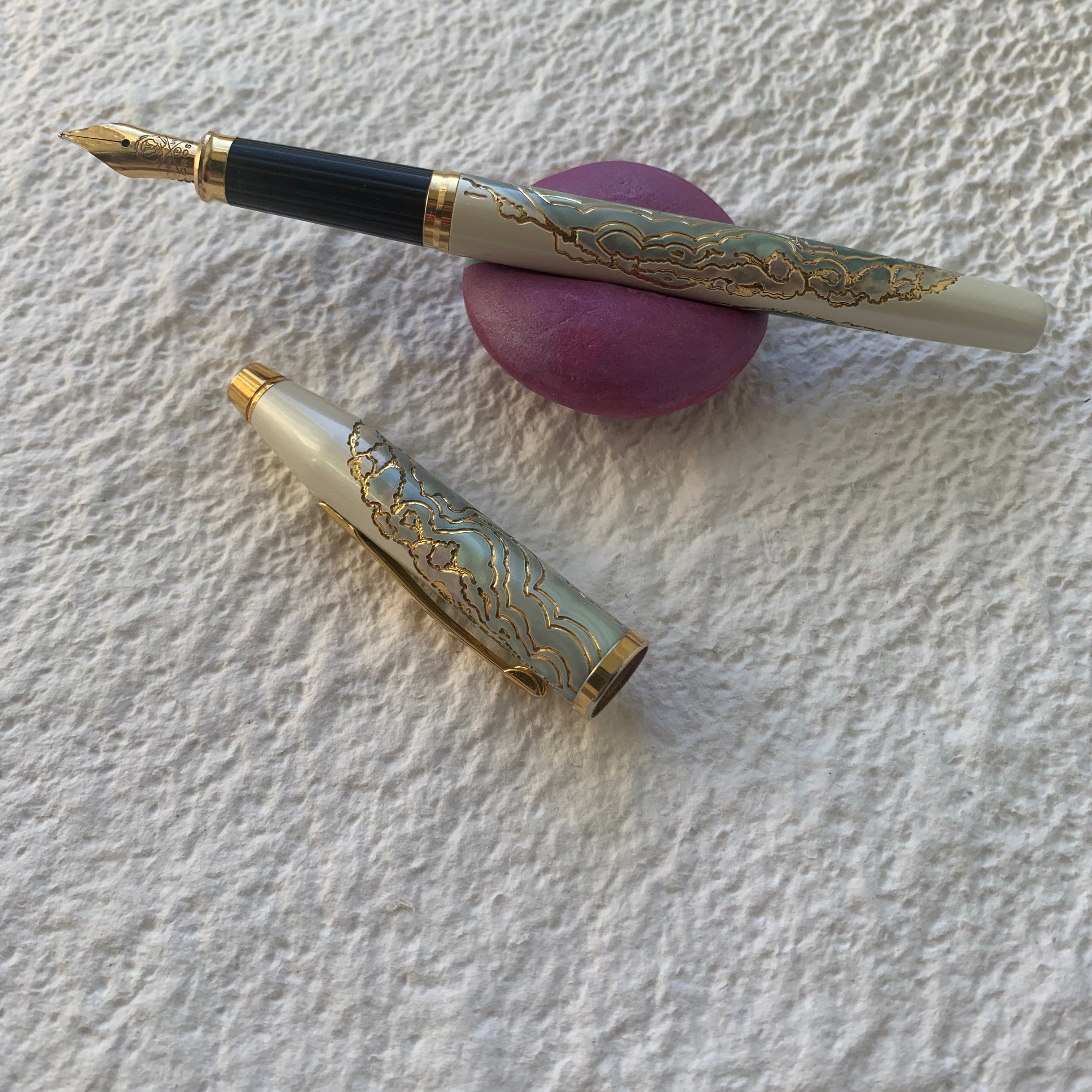 Decorative fountain pen and cap on a textured white surface with a pink pen rest, good for writers and journalling.